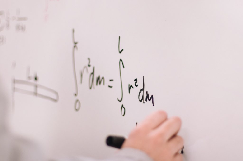 Image of someone writing complicated equations on a whiteboard